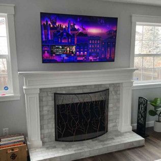 TV mounted above a fireplace with a decorative screen; windows on either side.