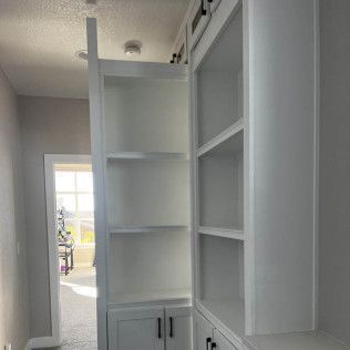 White built-in shelves and cabinets in a hallway, door frame visible, sunny window in the background.