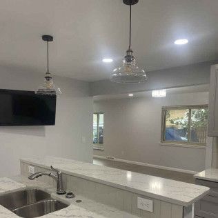 Kitchen with overhead lights, stainless steel sink, and a counter with a view into a dining area.