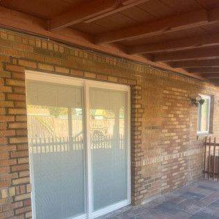 Brick wall with white sliding glass door and small window under a wooden beam roof.