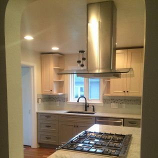 Kitchen with light cabinets, stainless steel range hood, stove, and a window.