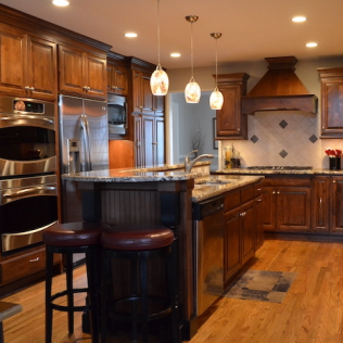 A kitchen with wooden cabinets and island, granite countertops, stainless steel appliances, and pendant lights.