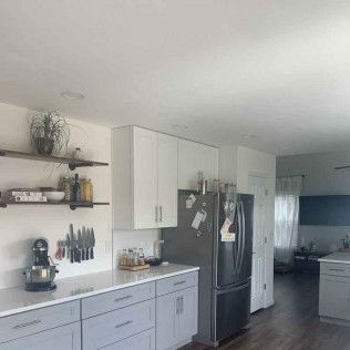 Kitchen with white cabinets, gray countertops, stainless steel refrigerator, and dark shelves.