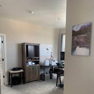 A room with a desk, cabinet, and art; white and gray walls, neutral colors.