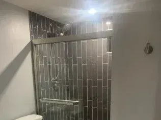 Shower with gray tiled walls and glass sliding door in a modern bathroom.