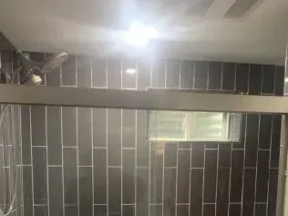 Dark gray tiled shower interior with a sliding glass door and a small window.