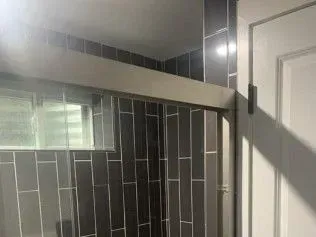 Shower with gray subway tile walls and a sliding glass door next to a white door.