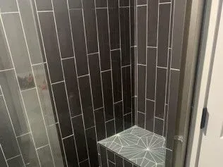 Dark tiled shower with a decorative bench.