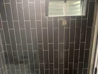 Dark rectangular tiles with white grout in a bathroom. A small window is centered.