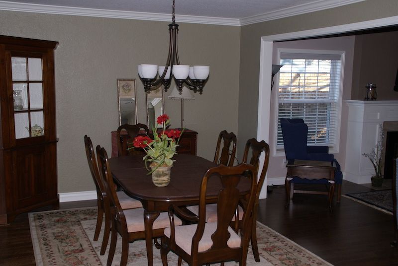 Dining room with oval table, chairs, chandelier, rug, and window. Dark wood furniture and neutral walls.