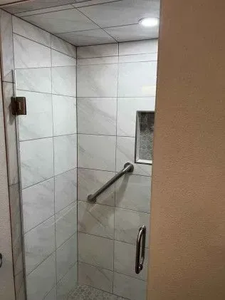 Tiled shower with glass door, grab bar, and small inset shelf.
