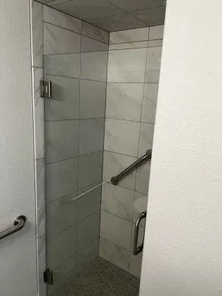 Glass shower stall with white tile walls and a handrail.