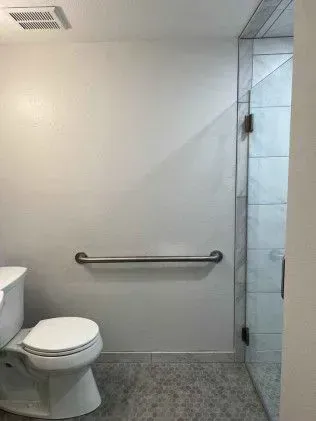 Bathroom with toilet, grab bar, and glass shower door. White walls, gray floor.