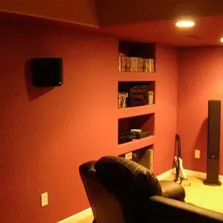 Red media room with built-in shelves and a black speaker. A black chair sits in front.