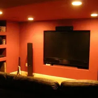 Home theater with red walls, large TV, black soundbar, and built-in shelving.