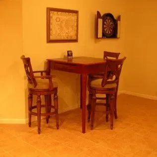 A small dining table with three chairs in a room with a dartboard and framed map.