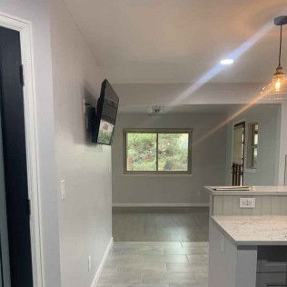 Hallway with TV mounted on wall; leads to a room with a window and a kitchen island.