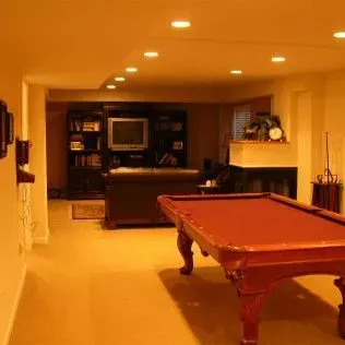 A red pool table in a basement.  There's a built-in entertainment center, a fireplace, and bright ceiling lights.