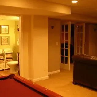 Basement with pool table, toilet, leather couch, and double doors. Yellow walls, tan floor.