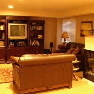 Cozy living room with brown leather sofa, built-in wooden entertainment center, fireplace, and window with blinds.