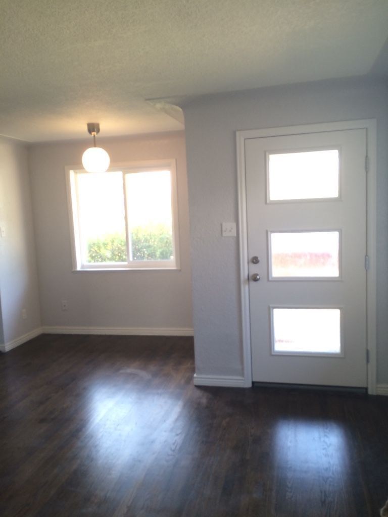 Interior of a room with dark wood flooring, light gray walls, and a white door with three glass panes.
