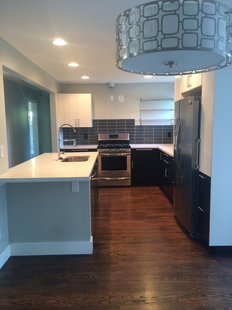Modern kitchen with white countertops, dark cabinets, stainless steel appliances, and a decorative light fixture.