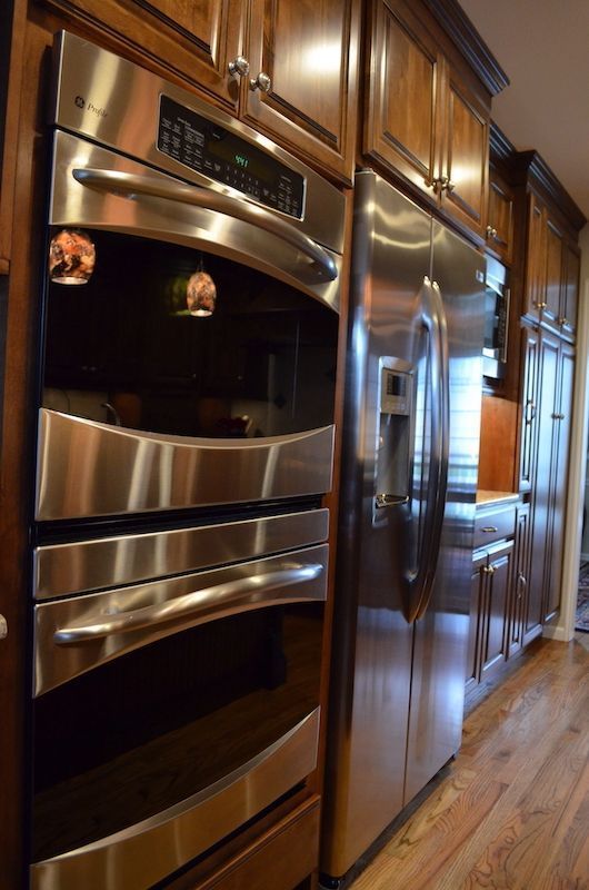 Stainless steel oven and refrigerator in a kitchen with wooden cabinets and floors.
