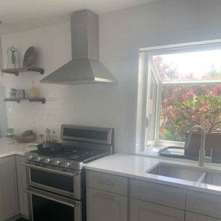 Kitchen with a stainless steel range hood, stove, window, and sink.