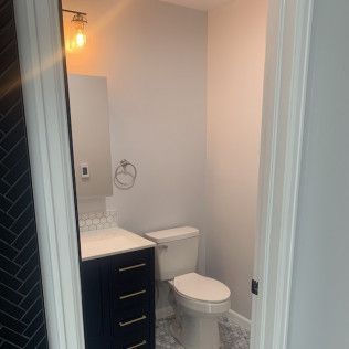 Small powder room with a navy vanity, white toilet, and gray walls.