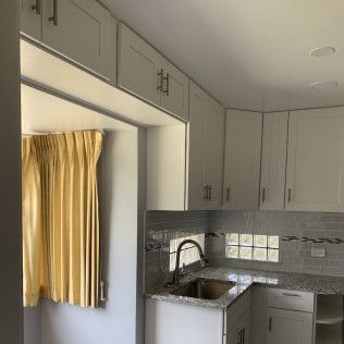 White kitchen cabinets with granite countertop; window with yellow curtain, stainless steel faucet.