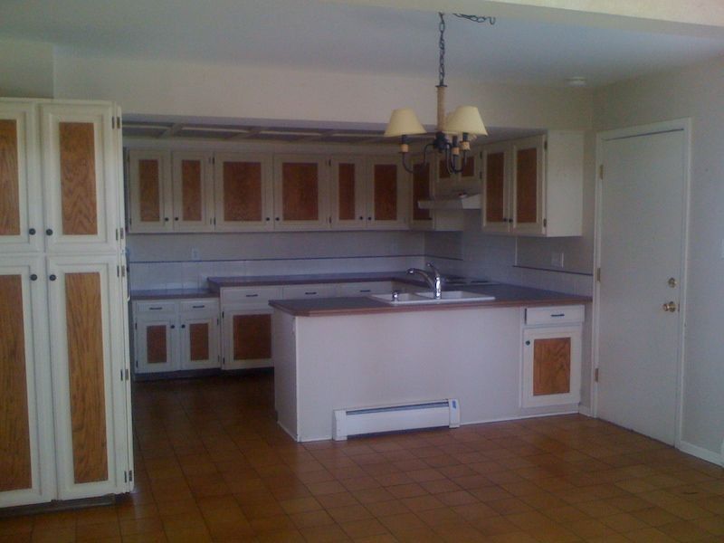 Kitchen with white cabinets, brown trim, and island. Brown tile floor.