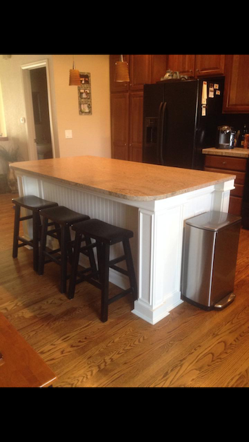 Kitchen island with white trim, wood countertop, black stools, and stainless steel trash can.