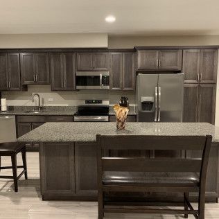 Kitchen with dark wood cabinets, stainless steel appliances, and a granite island with a bench.