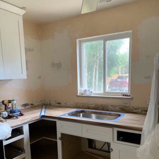 Kitchen under renovation, featuring a sink, cabinets, window, and countertop with blue tape.
