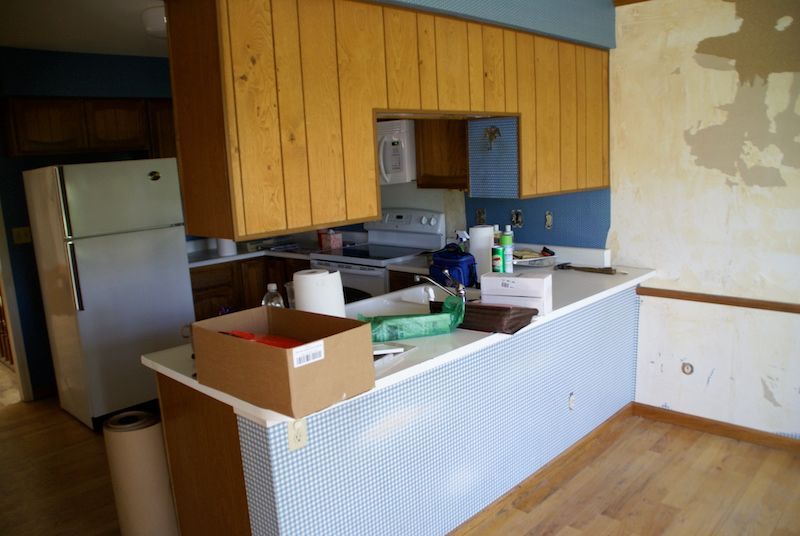 Kitchen renovation in progress, including cabinets, counter, refrigerator, and exposed wall.