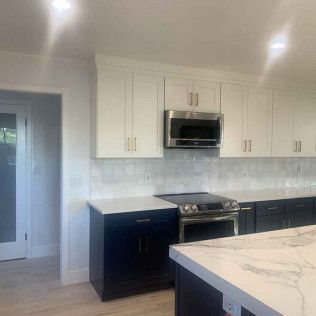 Kitchen with white upper cabinets, dark blue lower cabinets, stainless steel microwave, and marble countertops.