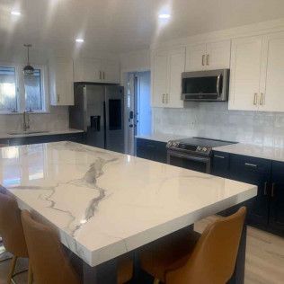 Modern kitchen with white and navy cabinets, large island with marble-look countertop, stainless steel appliances