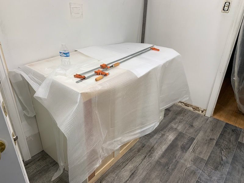 Cabinet with clamps, covered in plastic, in a room with gray flooring and white walls.