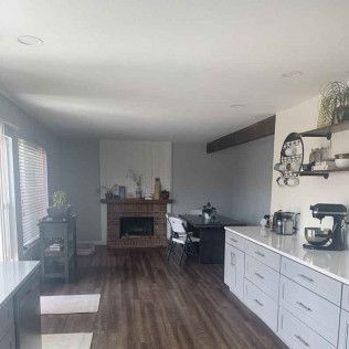 Open-concept kitchen and living room with fireplace, white cabinets, and wooden floors.