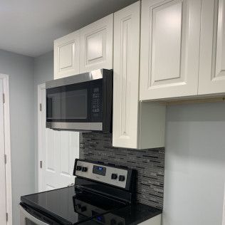 Kitchen with white cabinets, microwave above black stovetop, gray backsplash, and light blue walls.