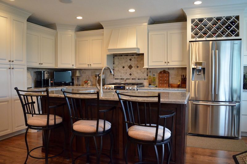 Kitchen with white cabinets, dark island, stainless steel refrigerator, and bar stools.