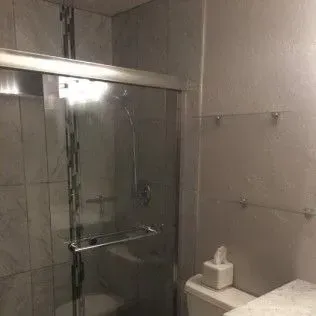 A bathroom with a sliding glass shower door and white walls. Toilet and tissue box are visible.