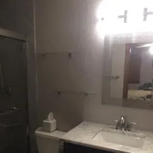 Bathroom with sink, mirror, and shower. Towel racks and tissue box present.