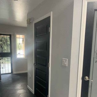 Hallway with black door, light gray walls, and black hexagonal tile floor.