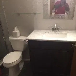 Bathroom with toilet, sink, mirror, and glass shelf.