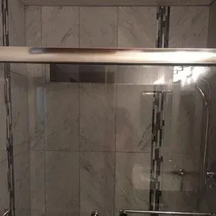 Shower stall with glass doors, white and gray tile, and chrome fixtures.