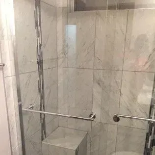 Shower with marble tile walls, a glass door, and chrome hardware.