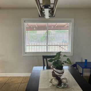 Dining room with table set with a centerpiece. Window with blinds in the background. Ceiling light above the table.