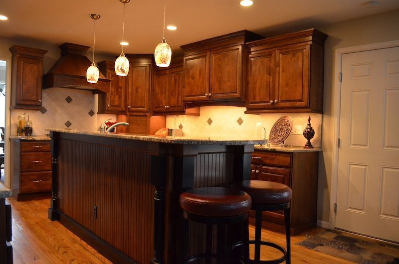 Kitchen with dark wood cabinets, island with stools, and pendant lights.