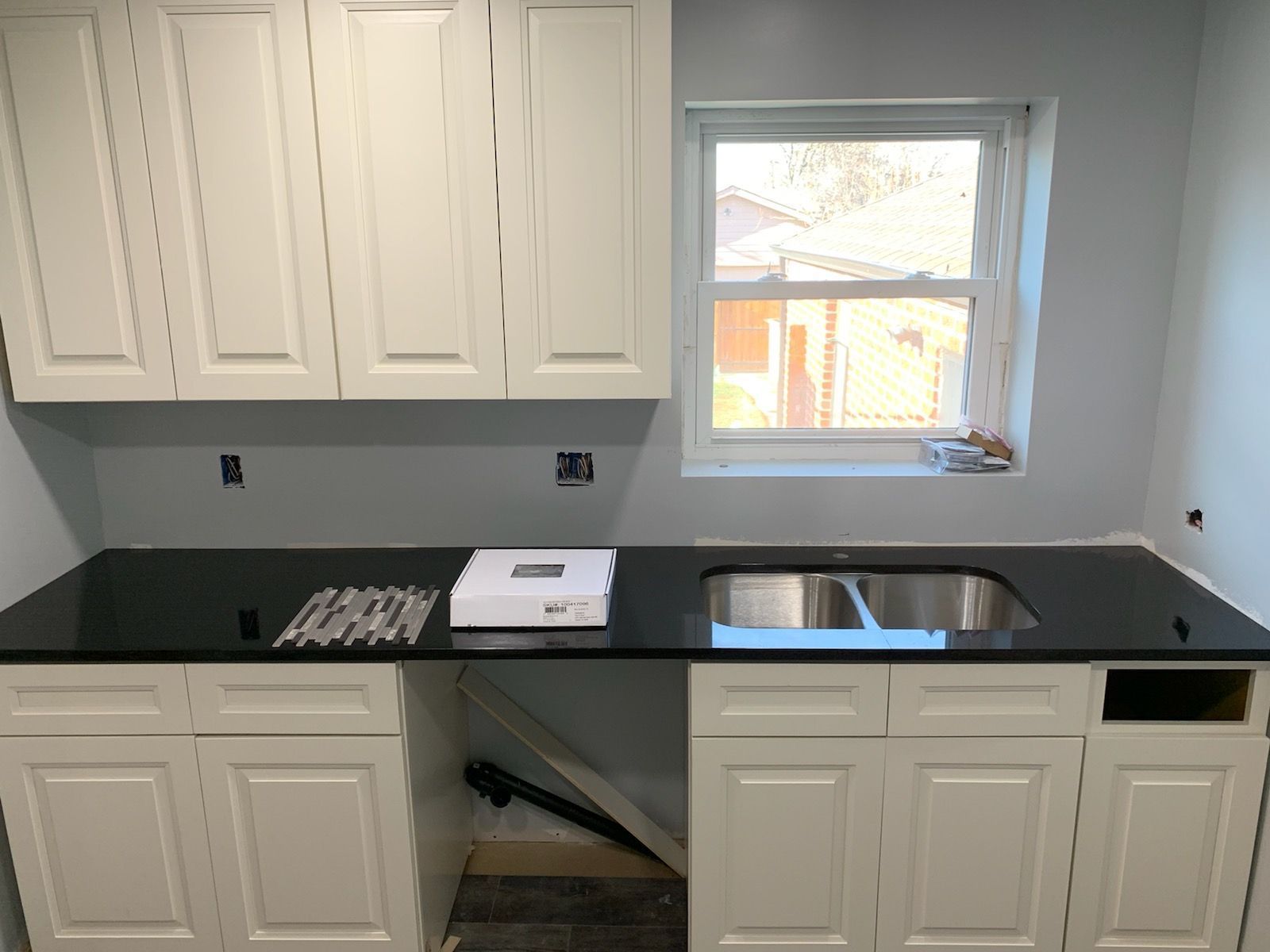 White kitchen cabinets with black countertop, stainless steel sink under a window.